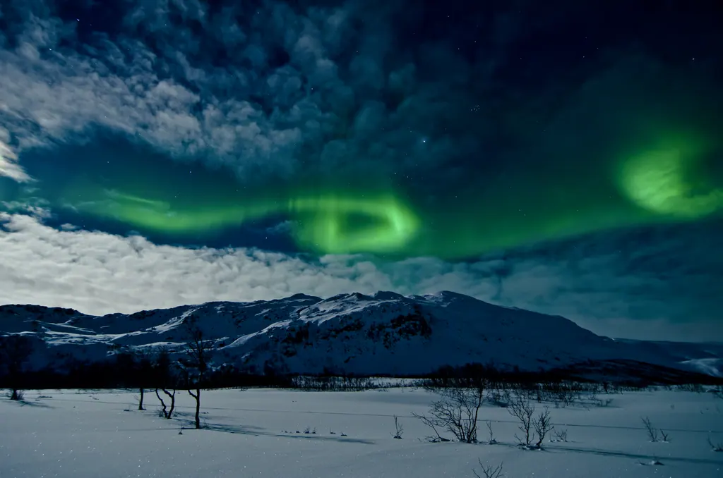 Grønt nordlys over snedækkede fjelde og en hvid sneslette ved Tromsø i Norge