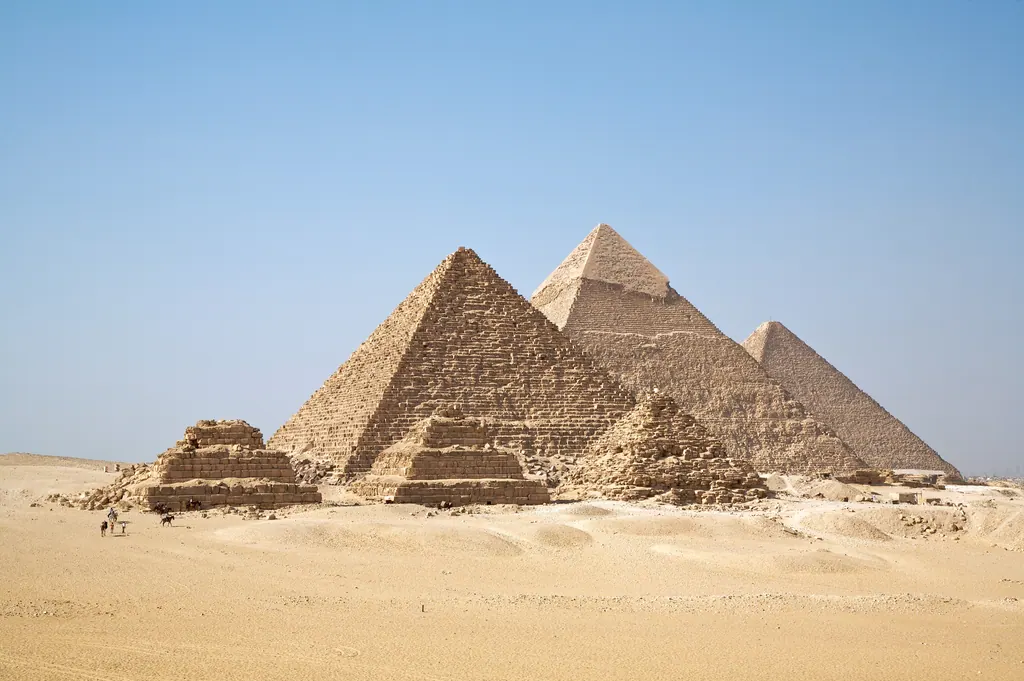 De tre store pyramider i Giza i ørkensand under en klar blå himmel