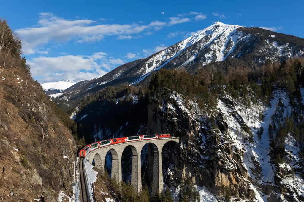 Glacier Express kører over Landwasser-viadukten i Schweiz med sneklædte bjerge i baggrunden