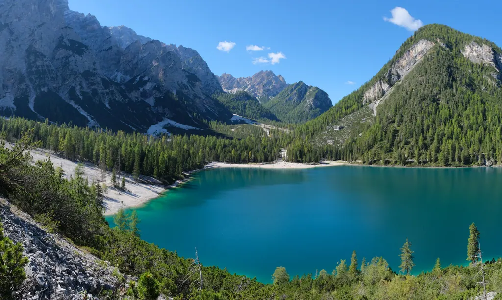 Turkis Lago di Braies omgivet af skov og høje kalkbjerge i Dolomitterne under blå himmel