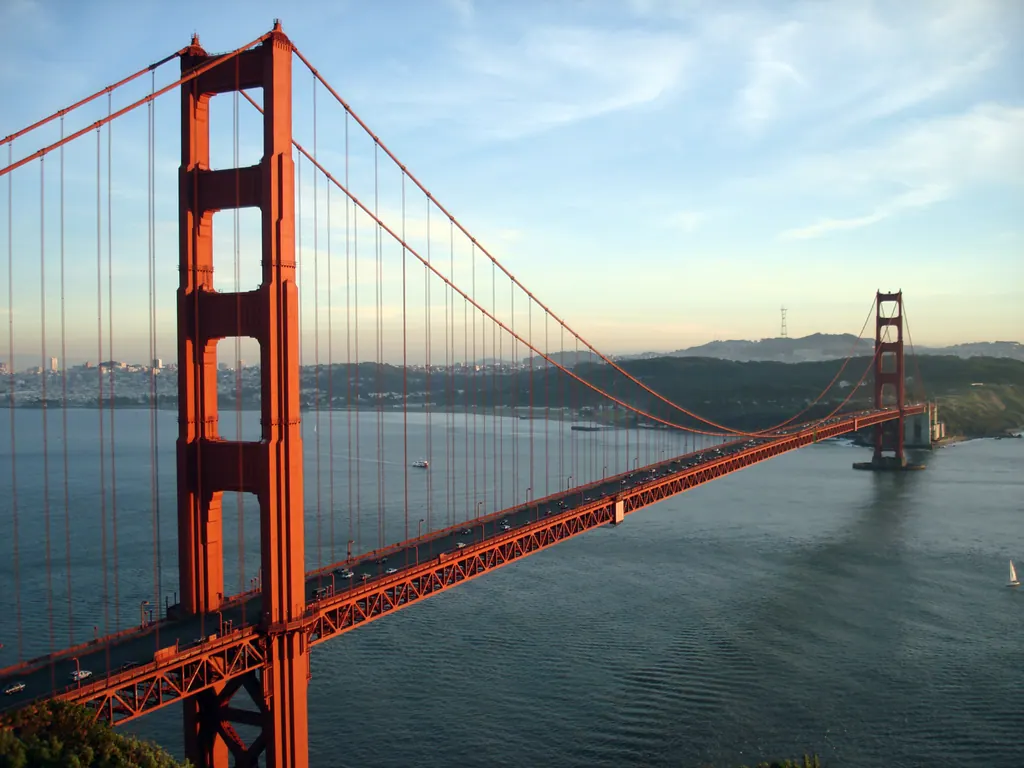 Golden Gate Bridge i solnedgang med San Franciscos skyline i baggrunden