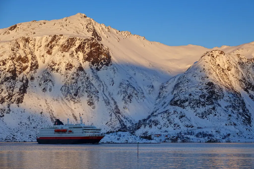 Hurtigrutens skib MS Kong Harald foran snedækkede fjelde ved Raftsundet i lavt vinterlys