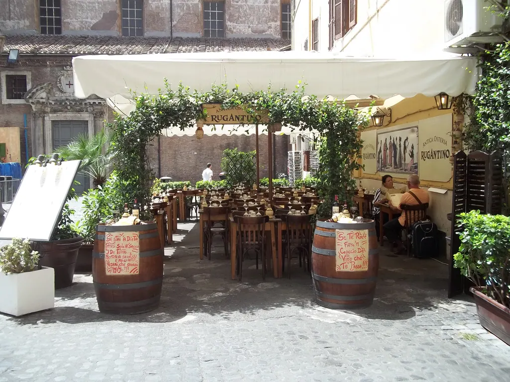 Udendørs borde under vinranker foran en lille restaurant i en brostensgade i Trastevere i Rom