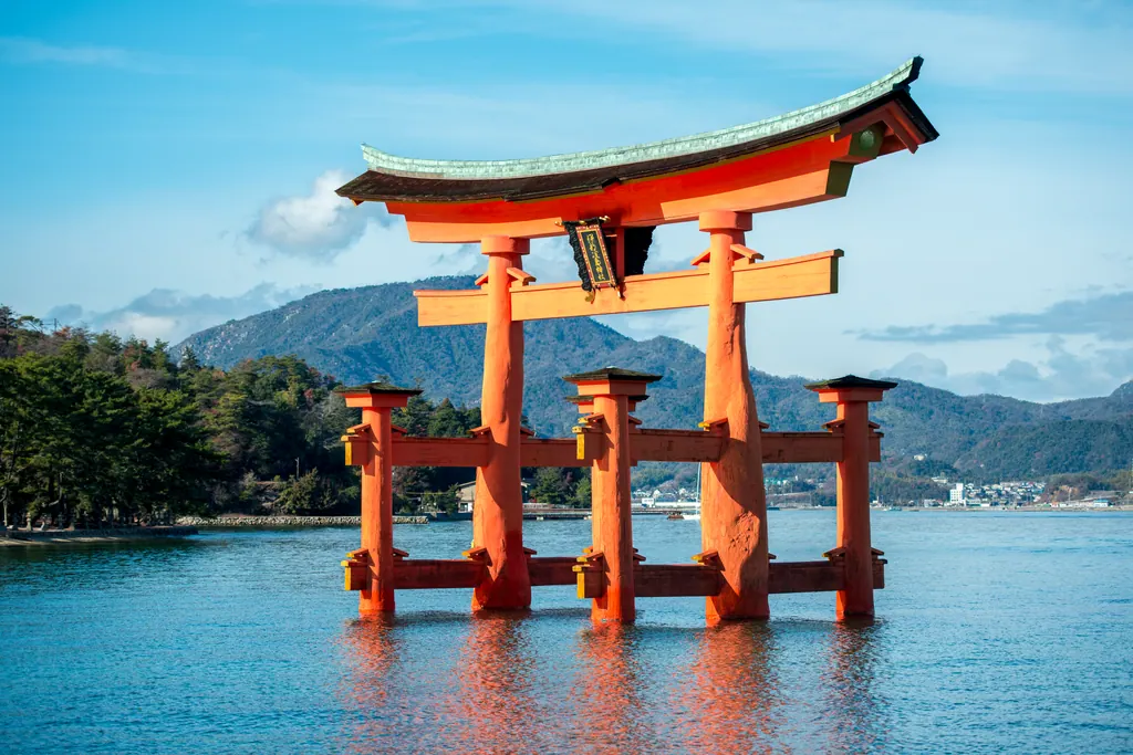 Den røde torii-port ved Itsukushima-helligdommen står i vandet ud for Miyajima med grønne bjerge i baggrunden