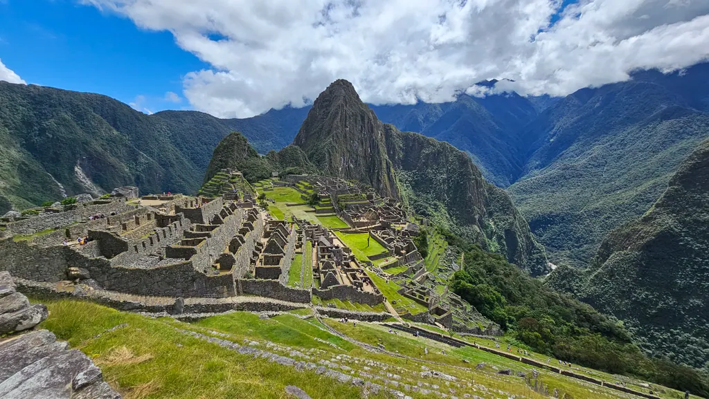 Inkabyen Machu Picchu med grønne terrasser og bjerget Huayna Picchu under en blå himmel med hvide skyer