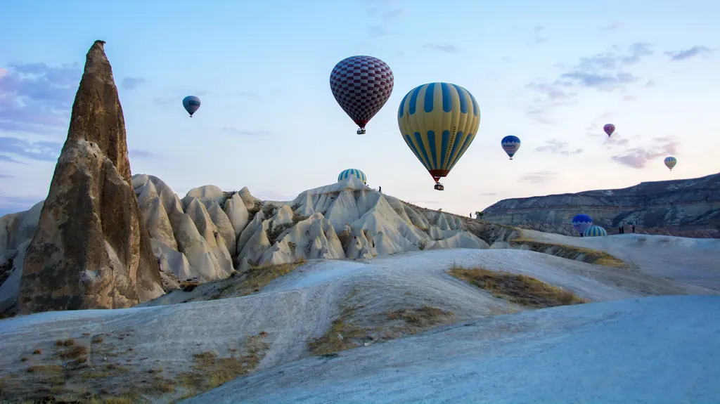 Farverige luftballoner over hvide klippeformationer i Kappadokien ved solopgang