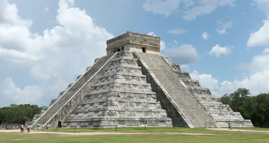 Chichén Itzá med den store pyramide El Castillo på en græsslette under blå himmel