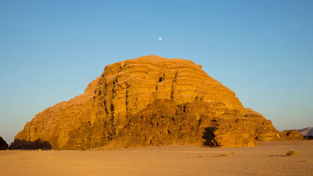 Sandstensbjerg i Wadi Rum lyser gyldent i aftensolen over rødt ørkensand