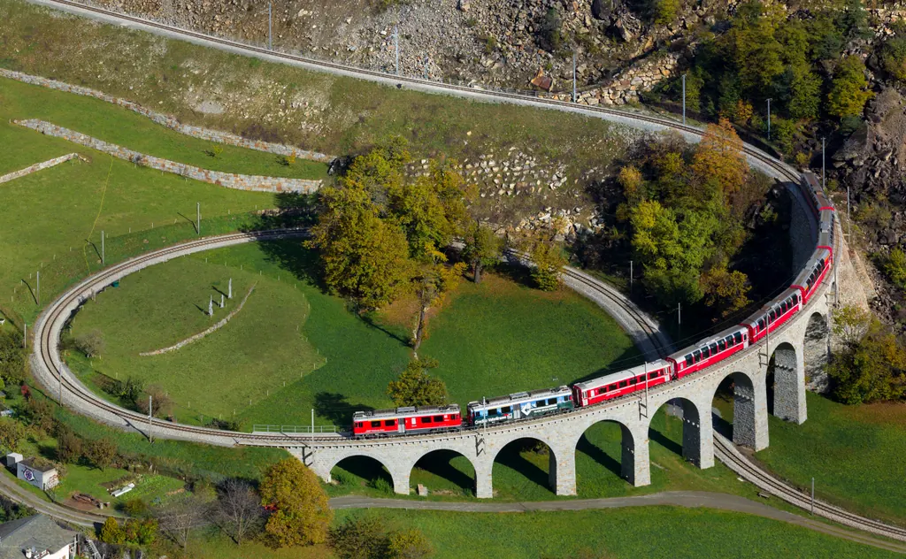 Et rødt tog kører over den cirkelformede viadukt ved Brusio på Berninabanen