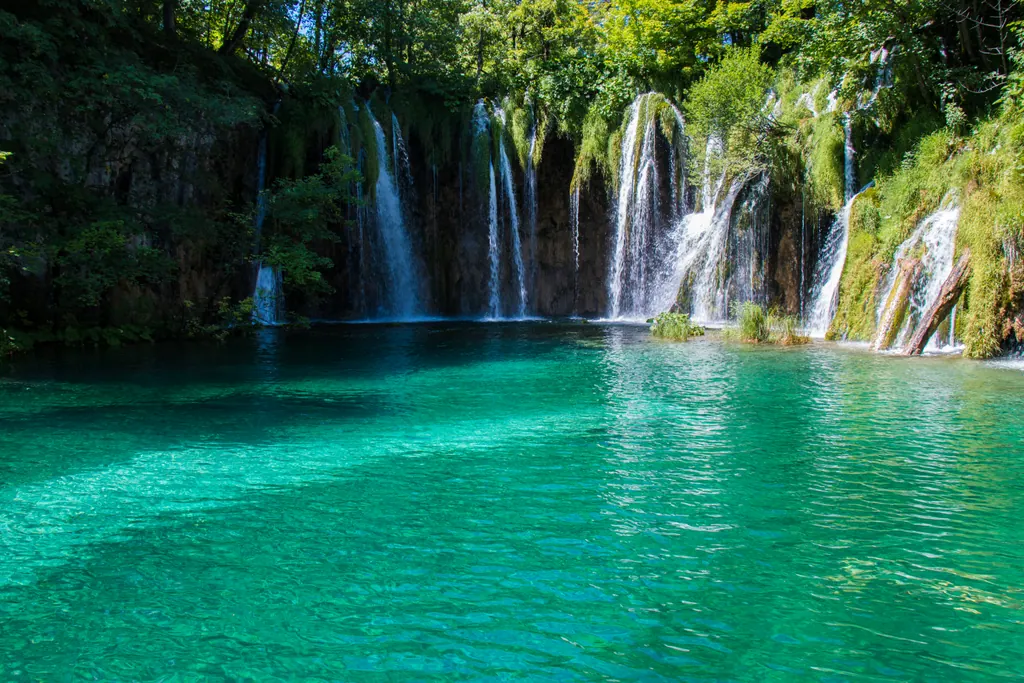 Vandfald falder ned i en turkis sø omgivet af grøn skov i Plitvice-søernes nationalpark