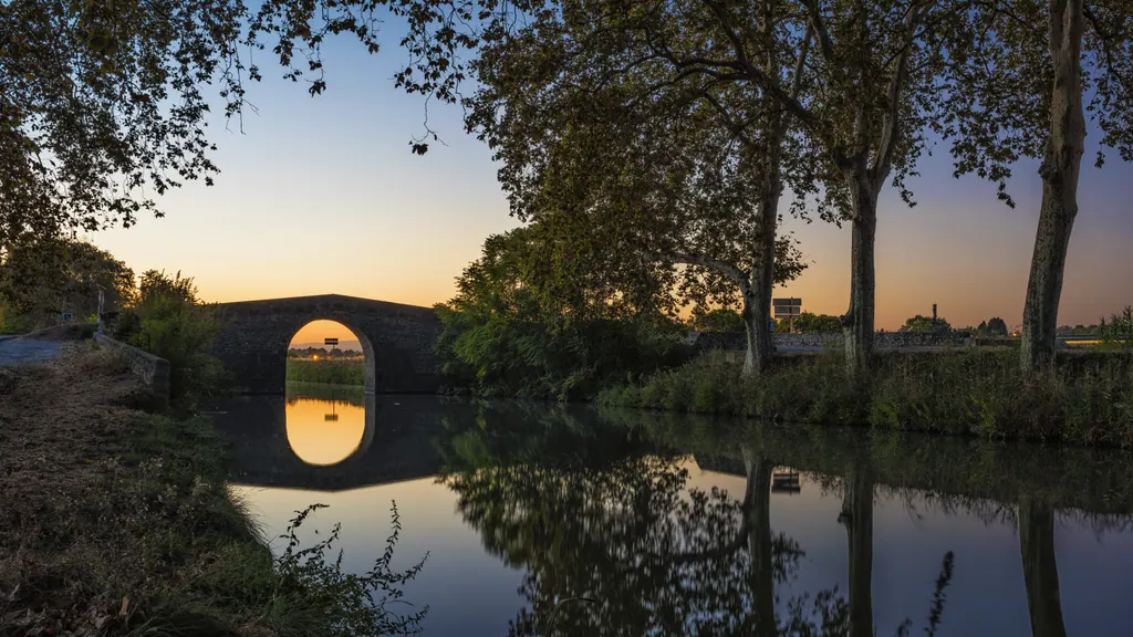 Caylus-broen spejler sig i Canal du Midi ved Villeneuve-lès-Béziers i aftenlys