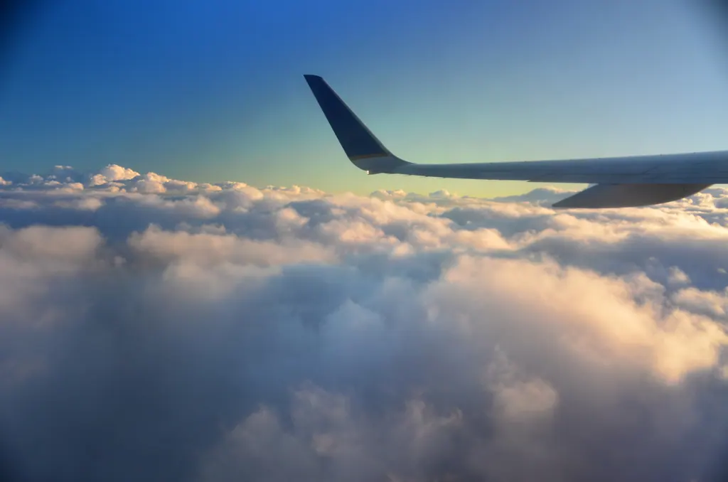 Udsigt fra et flyvindue med en flyvinge over et hav af gyldne skyer i solnedgangslys