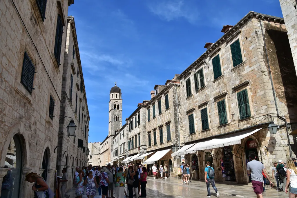 Den brolagte hovedgade Stradun i Dubrovniks gamle bydel med stenhuse, grønne skodder og mange gående under en blå himmel