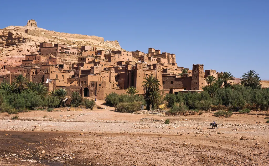 Lerbyen Aït Benhaddou på bakken over palmer og grønne marker under en klar blå himmel i Marokko