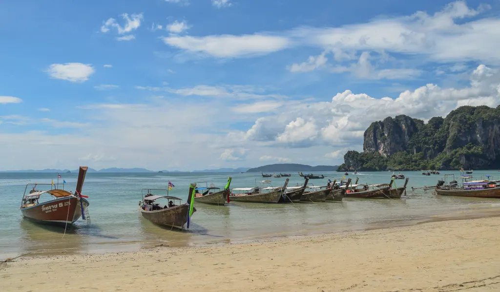 Langhalebåde ved den lyse sandstrand West Railay i Krabi med kalkstensklipper og turkis hav