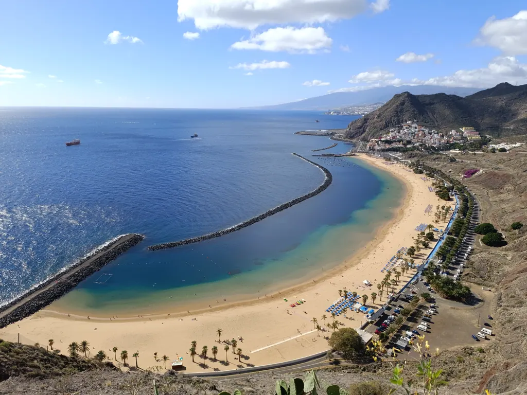 Den lyse sandstrand Las Teresitas på Tenerife med bølgebryder, blåt hav og bjerge bag ved