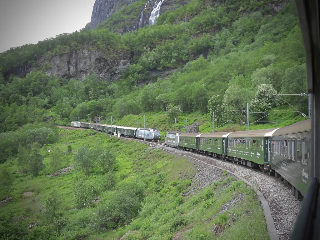 To tog mødes på Flåmsbanen i den grønne Flåmsdal med et vandfald over klippen