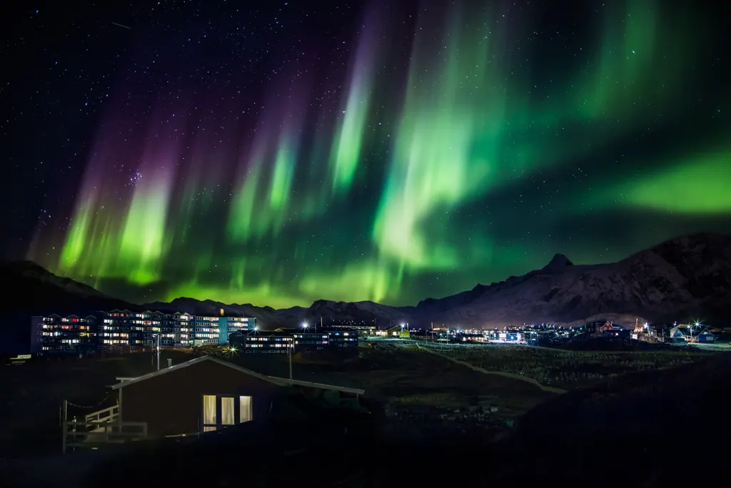 Kraftigt grønt og violet nordlys over en by i Grønland