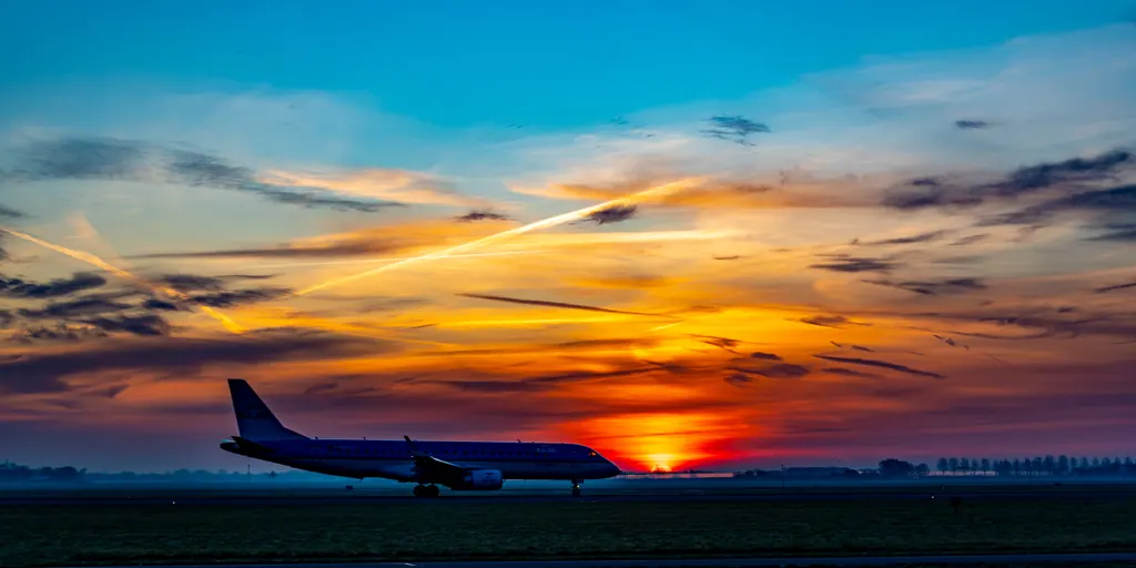 Solopgang over en lufthavn med et passagerfly på landingsbanen og en himmel i orange og blå