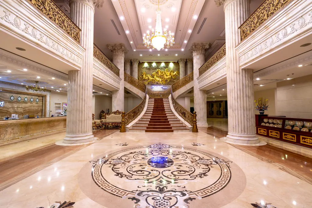 Lobby i et luksushotel med marmorgulv, søjler, lysekrone og bred trappe med rød løber