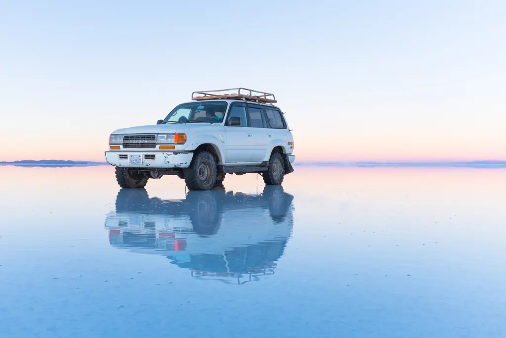 Firehjulstrækker spejler sig i vandet på Salar de Uyuni i skumringen